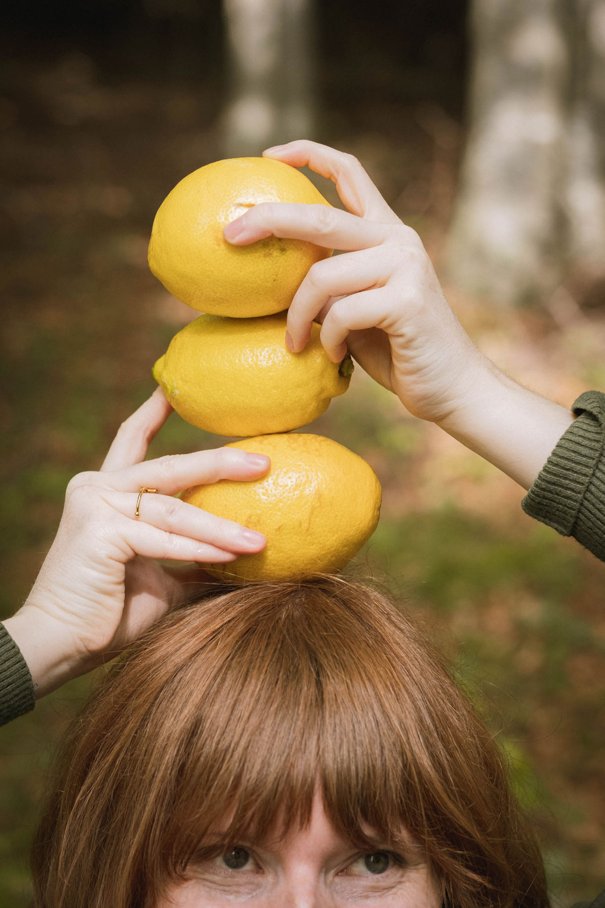 Zwei Hände stapeln drei Zitronen auf dem Kopf einer Frau (Branding-Symbol)